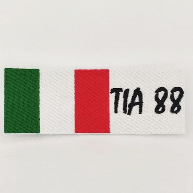 Fotografia di una toppa ricamata della bandiera dell'Italia con la scritta TIA 88 nera