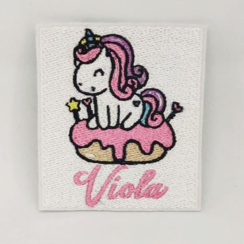 Fotografia di una toppa ricamata di un unicorno su una ciambella glassata con sotto il nome "Viola"