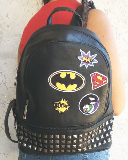 Fotografia ragazza di spalle con zaino di pelle nero con borchie con diverse toppe a tema fumetto e Batman