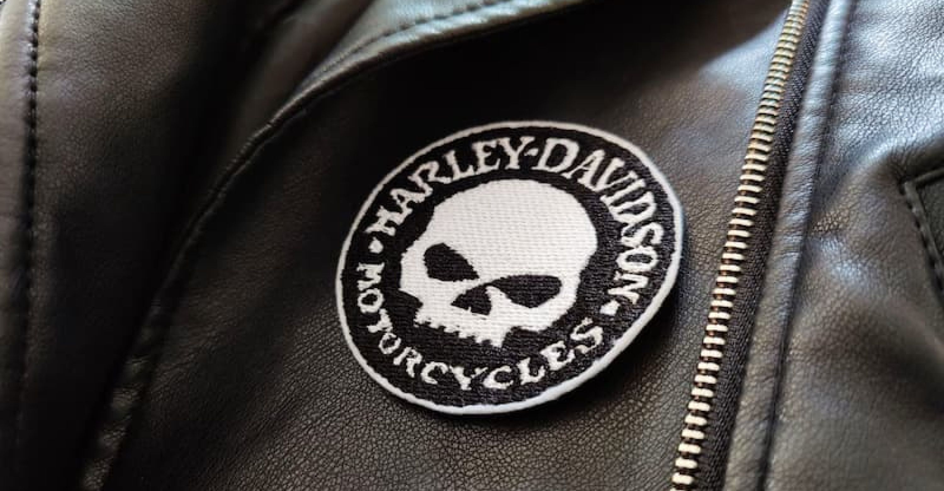 Fotografia di un dettaglio di un giubbotto di pelle nero con toppa rotonda nera con teschio e scritta Harley-Davidson Motorcycles